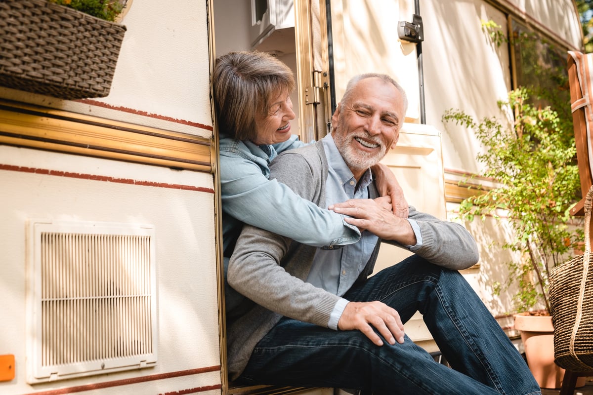 Happy loving elderly senior couple hugging embracing cuddling together while on a trip adventure holiday in trailer camper van caravanning in motor wheel home