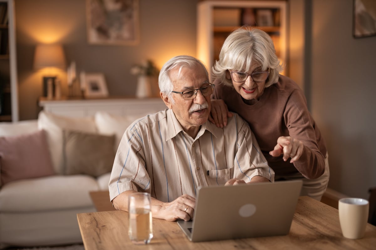 Senior couple at home exploring a laptop screen together, one partner guiding the other